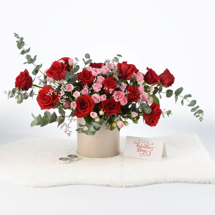 Vibrant red and pink roses in beige cylinder vase with Valentine’s card.