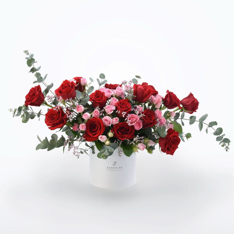 Vibrant red and pink roses with eucalyptus in sleek white Zuvees box, perfect gift.