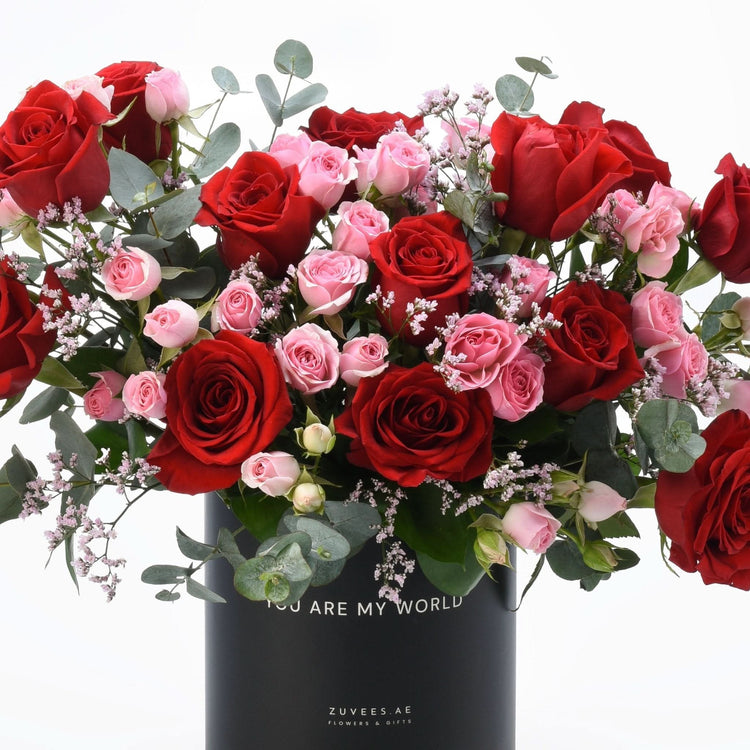 Vibrant red and pink roses cascade in sleek black vase with “You Are My World” inscription.