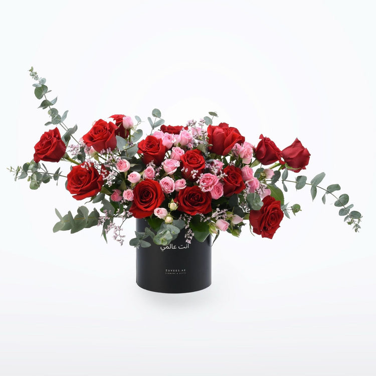 Vibrant red and pink roses with eucalyptus in sleek black cylindrical vase.