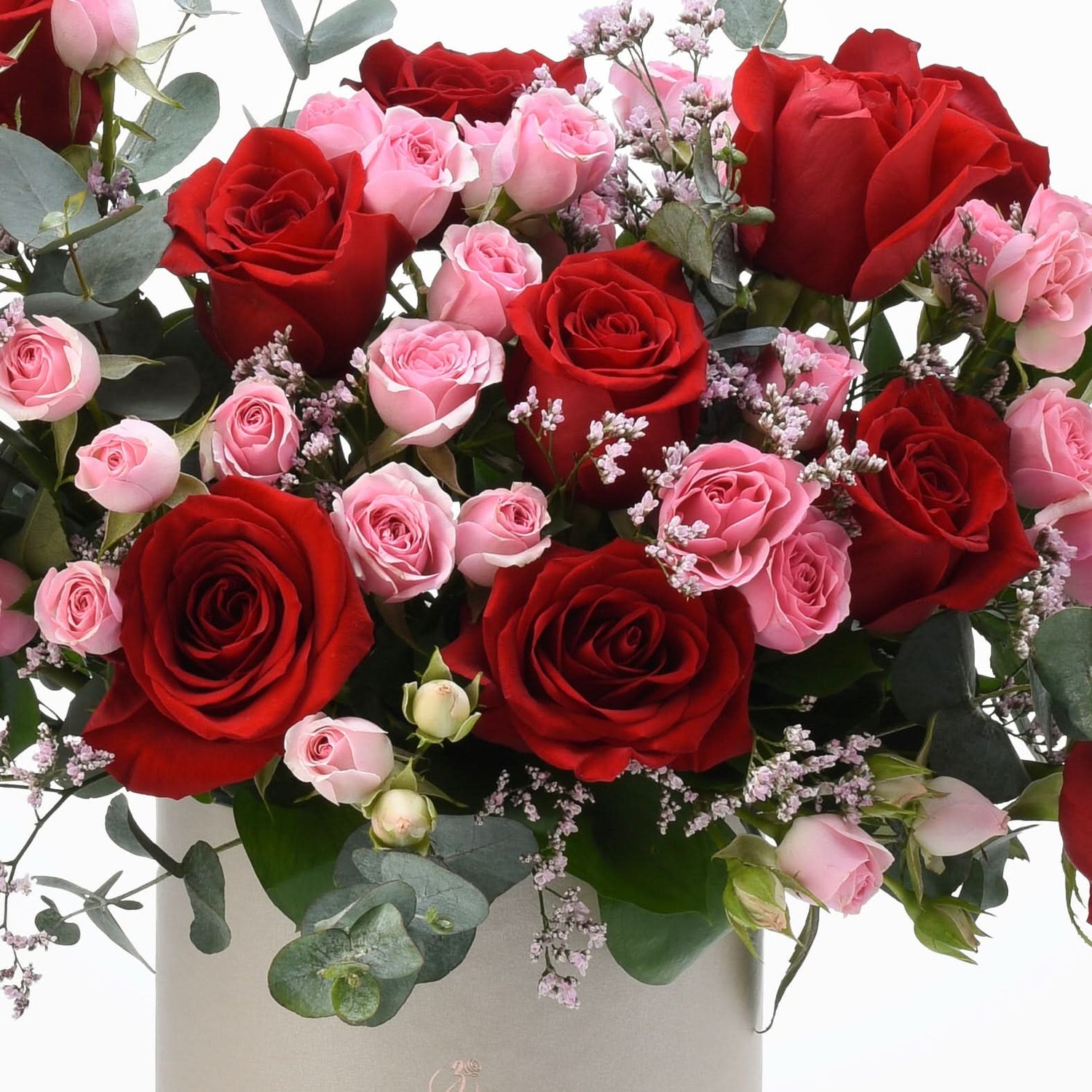 Vibrant red and pink roses with eucalyptus, baby’s breath, in elegant gray box.