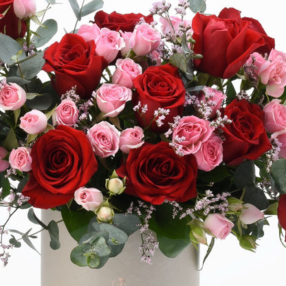 Vibrant red and pink roses with eucalyptus, baby’s breath, in elegant gray box.