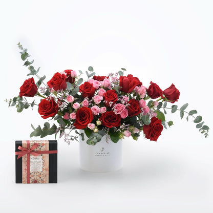 Vibrant red and pink roses with eucalyptus in white Zuvees box, paired with patterned gift box.