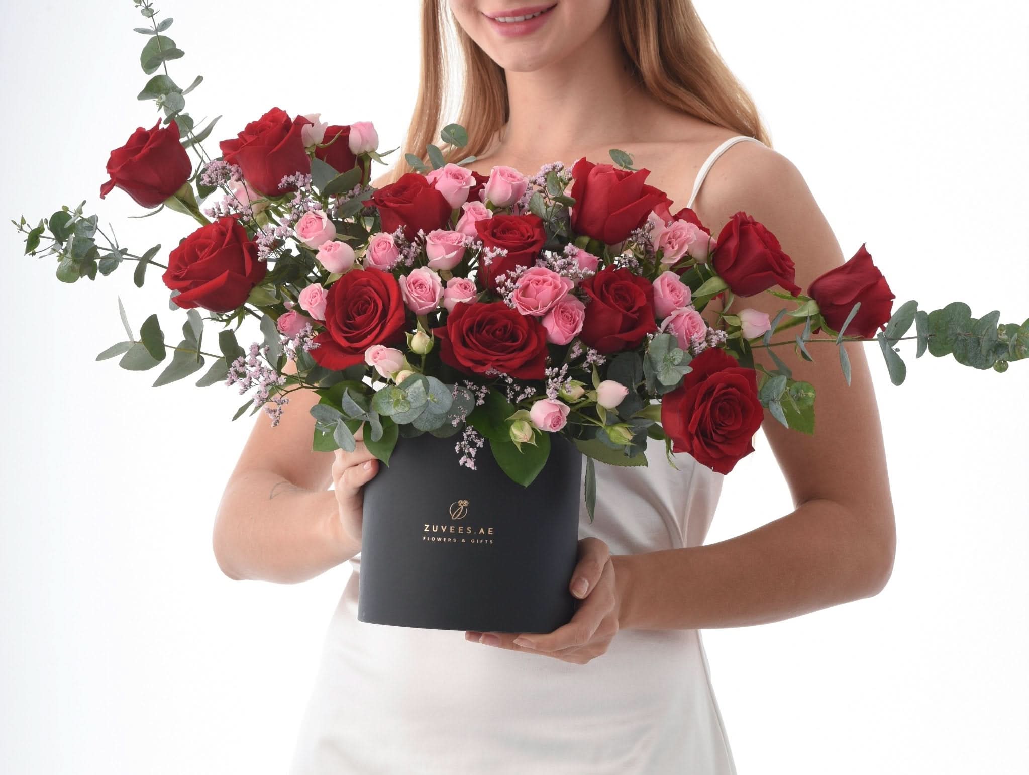 Woman holds black box of red and pink roses with eucalyptus, elegant gift presentation.