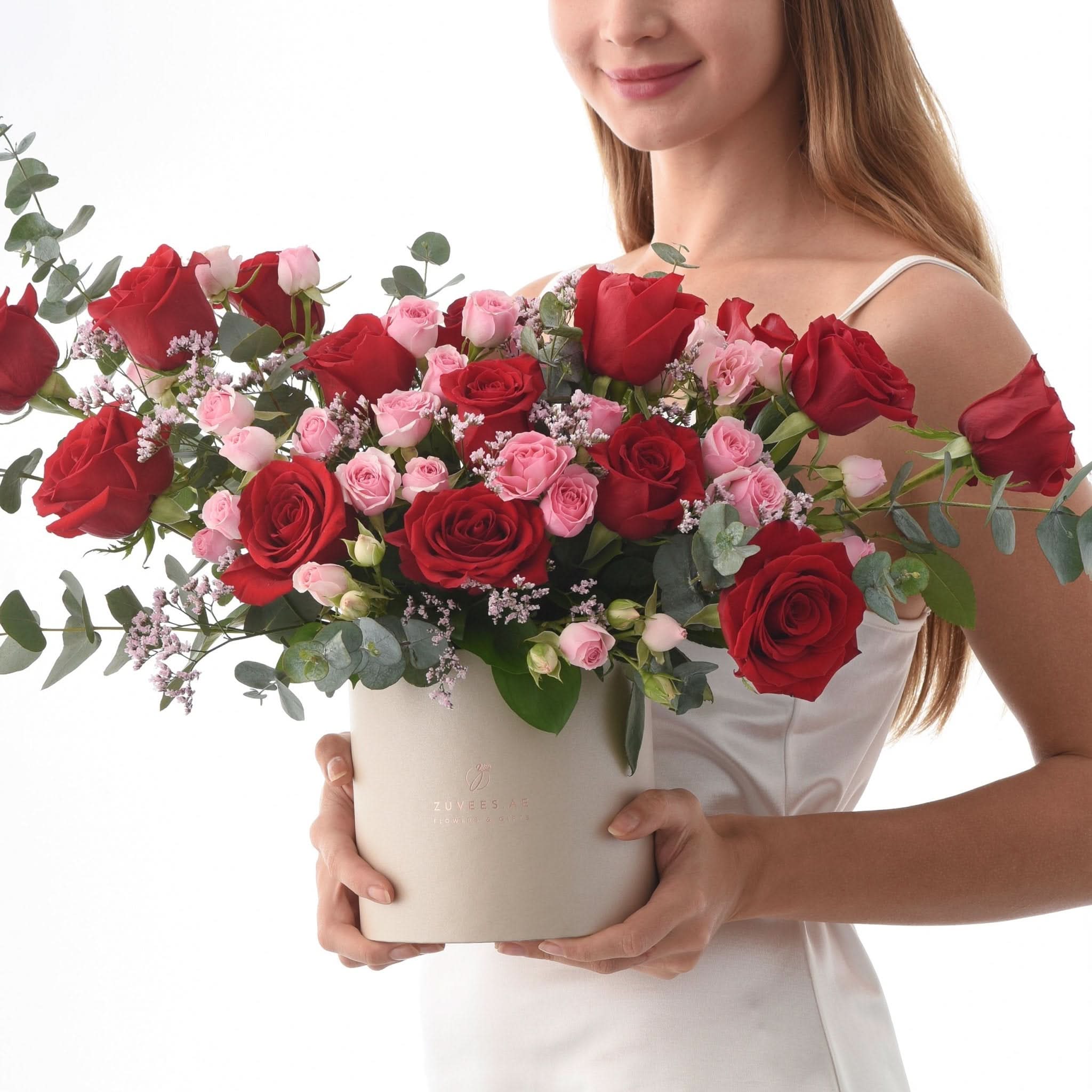 Woman holds lush red and pink rose bouquet in beige box.