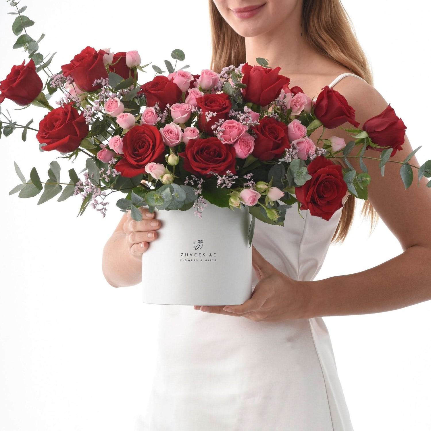 White box holds lush red and pink roses with eucalyptus, elegant gift presentation.