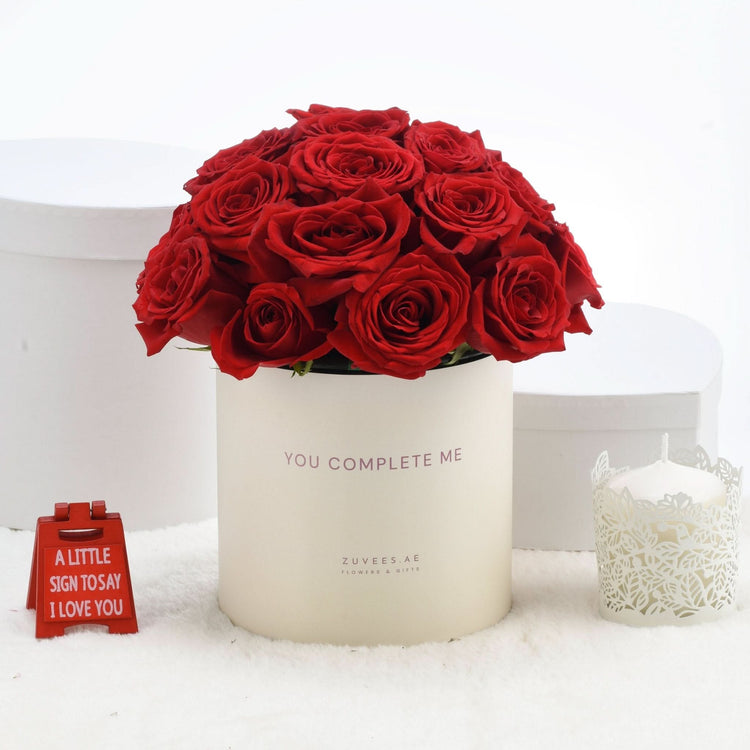 Vibrant red roses in cream box with “You Complete Me” text, romantic gift setup.