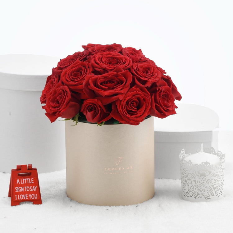 Vibrant red roses in beige box, beside "I love you" sign and lace candle.