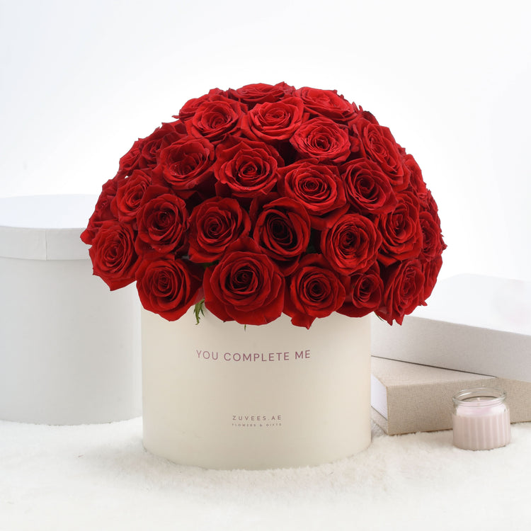 Vibrant red roses in cream box reading "You Complete Me".