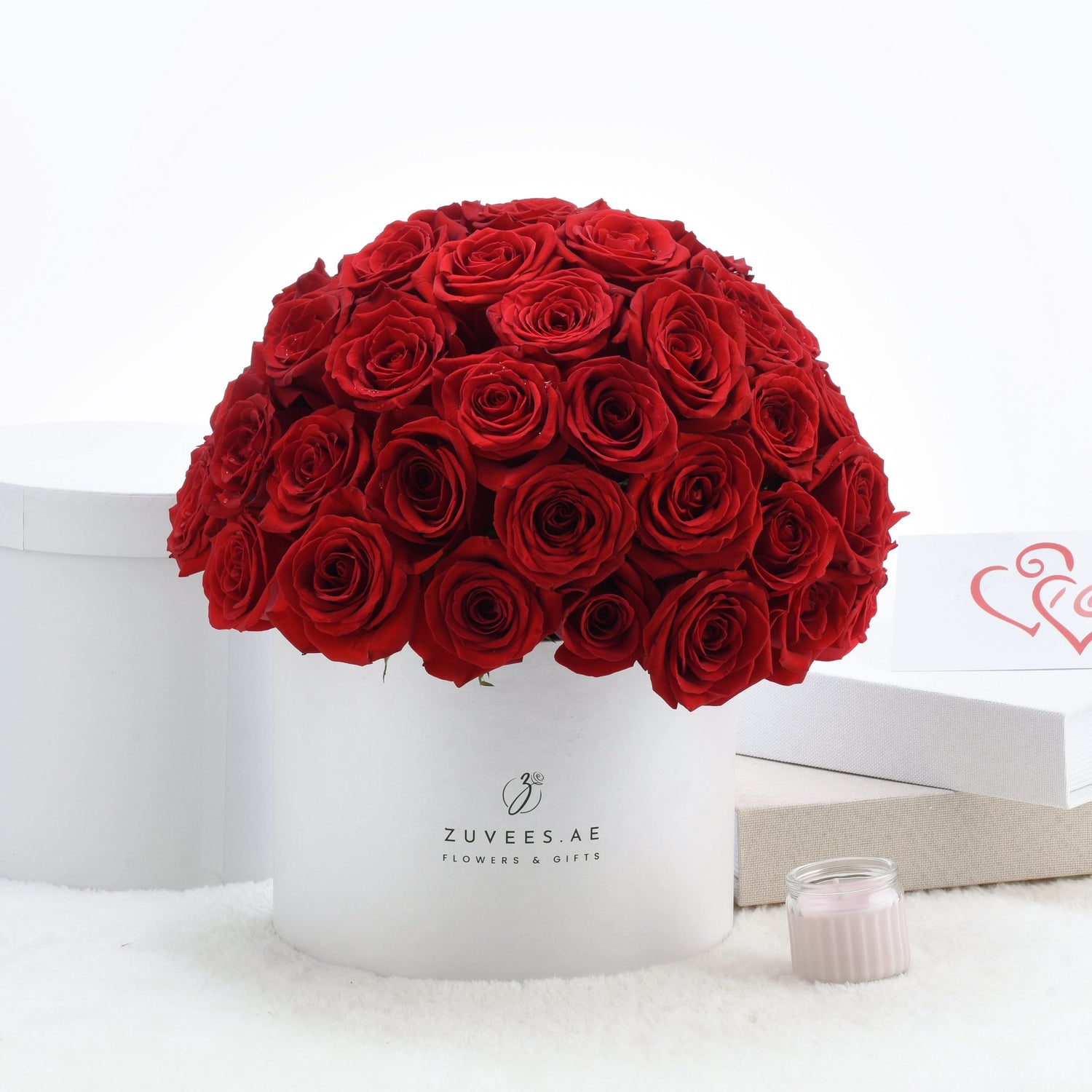 Vibrant red roses in white cylindrical box with elegant branding.