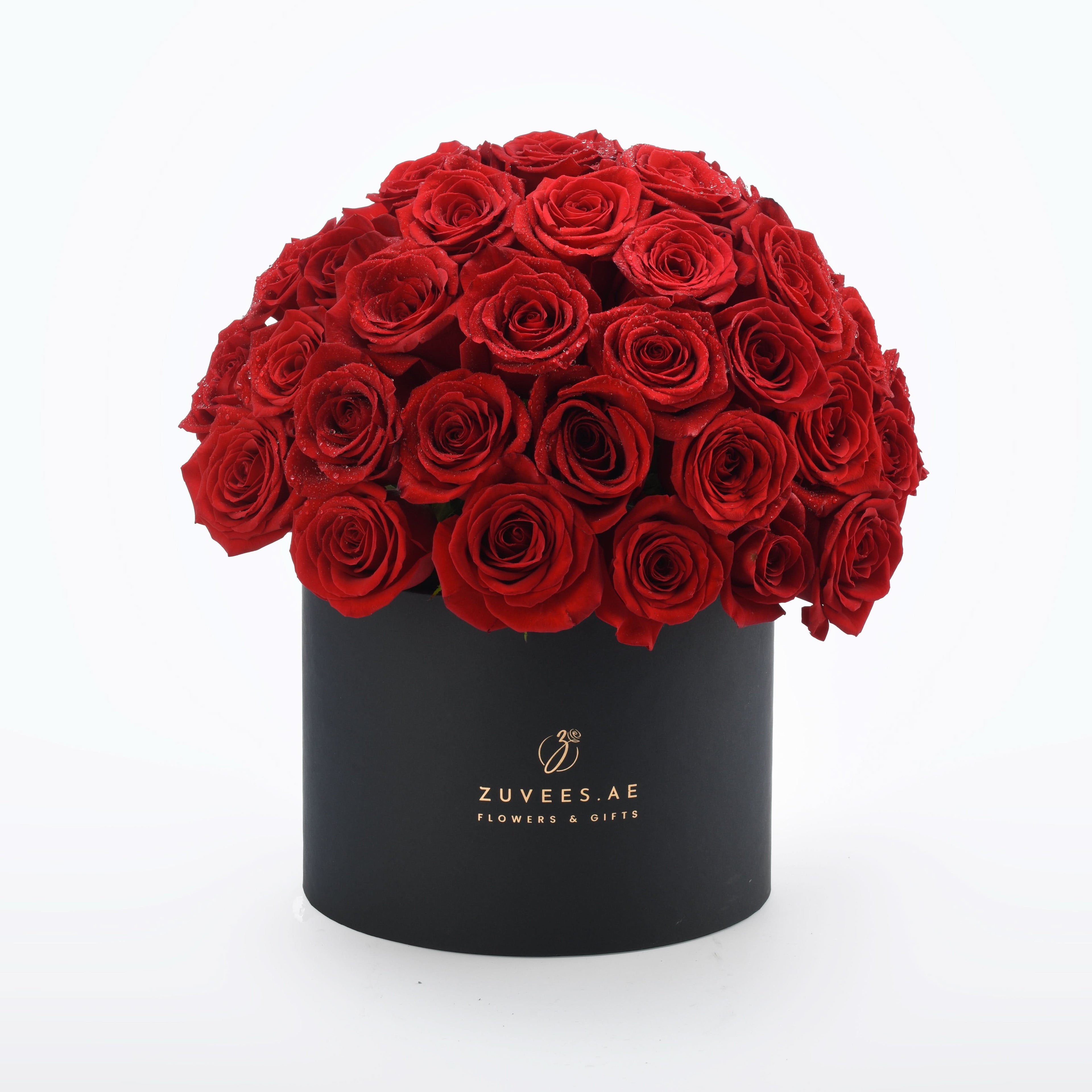 Vibrant red roses cascade from sleek black box with gold branding.