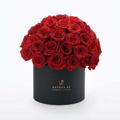 Vibrant red roses cascade from sleek black box with gold branding.