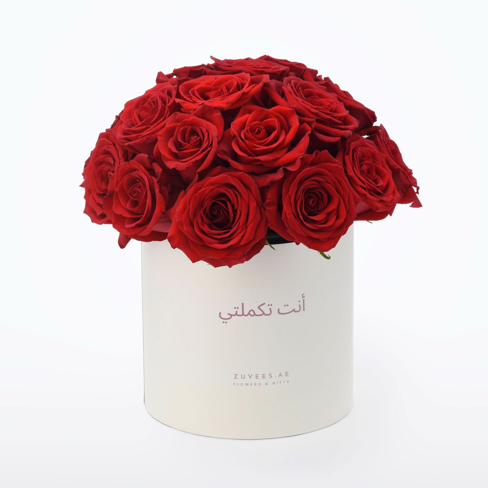 Vibrant red roses overflowing from a cream cylinder box with Arabic script.