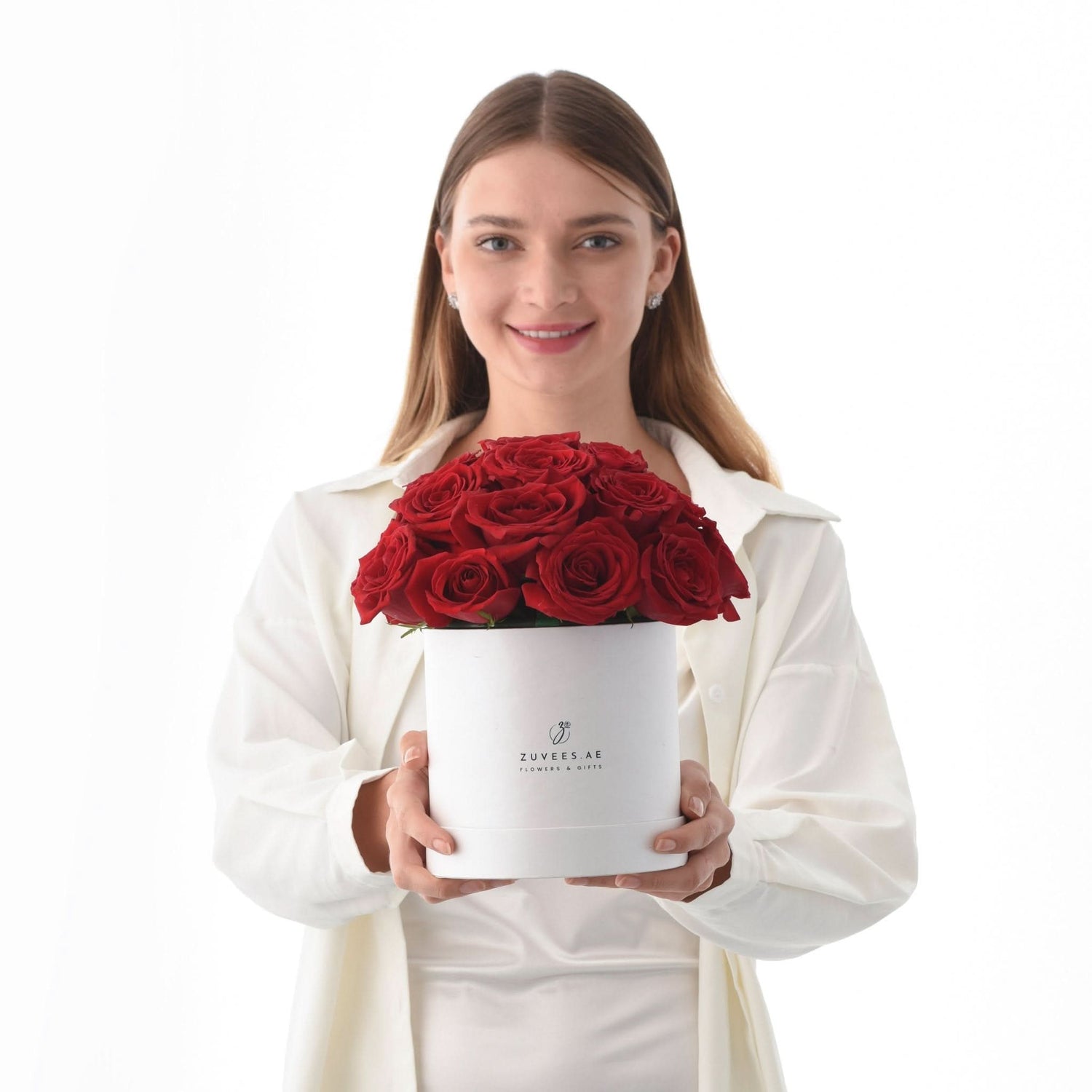 Woman holds white box overflowing with vibrant red roses against clean white background.