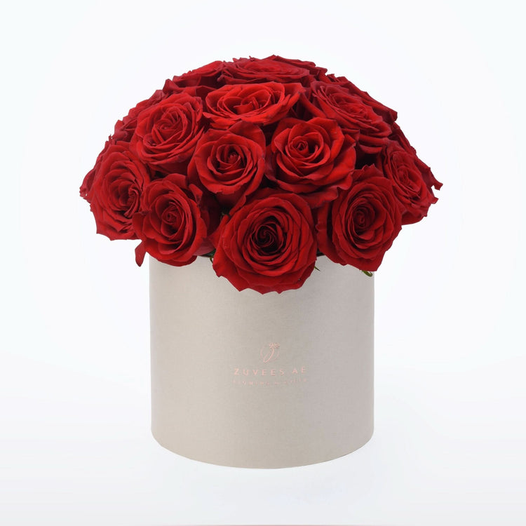 Vibrant red roses overflowing from a sleek beige cylindrical box.
