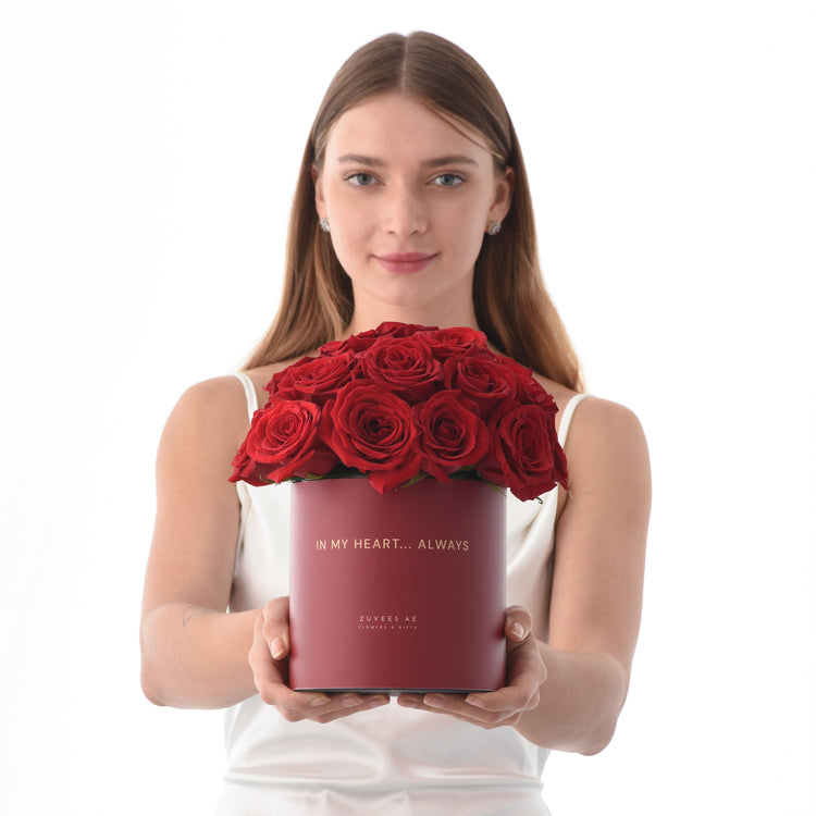 Woman holds matte red box of vibrant red roses with gold "In My Heart... Always" inscription.