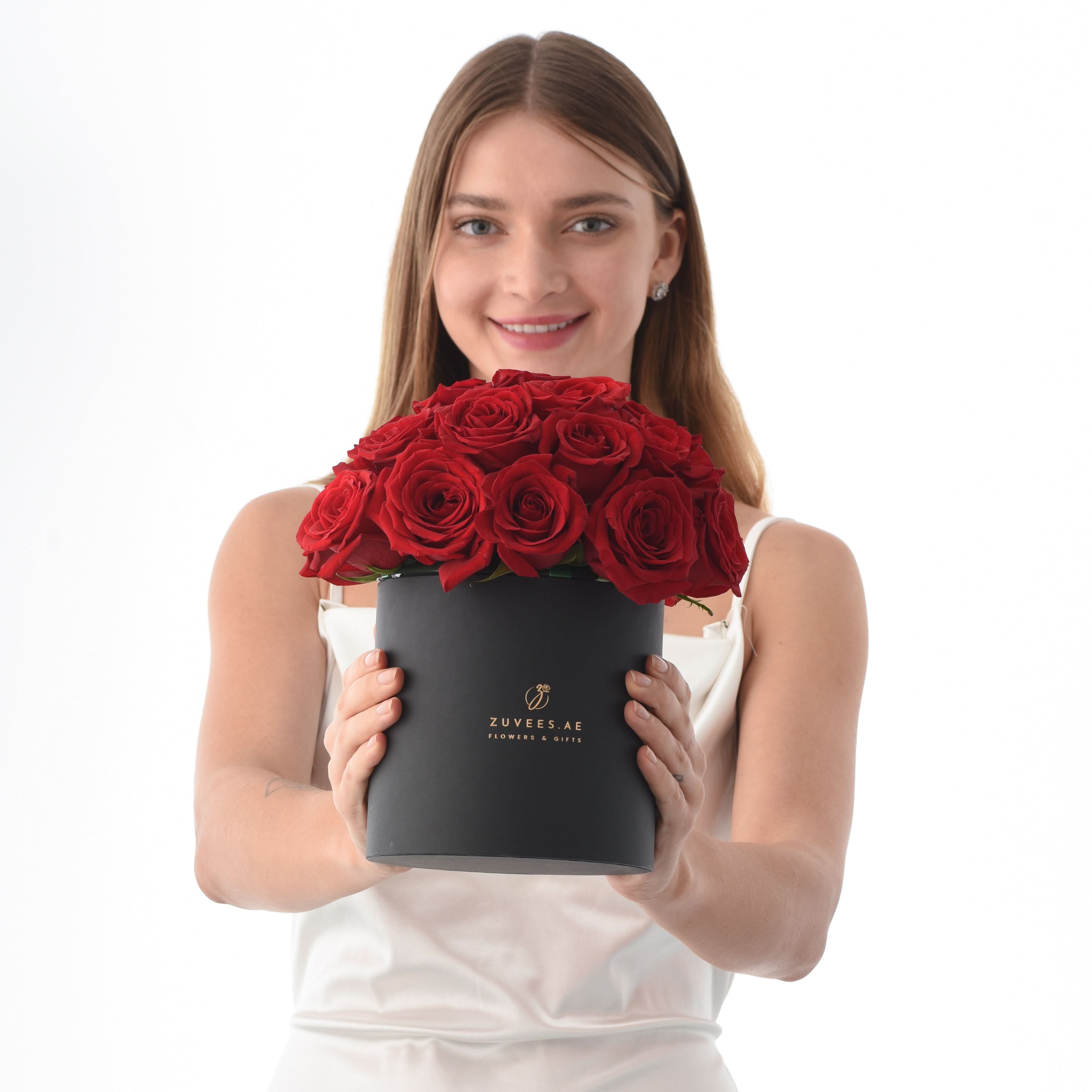 Woman holds black box overflowing with vibrant red roses.