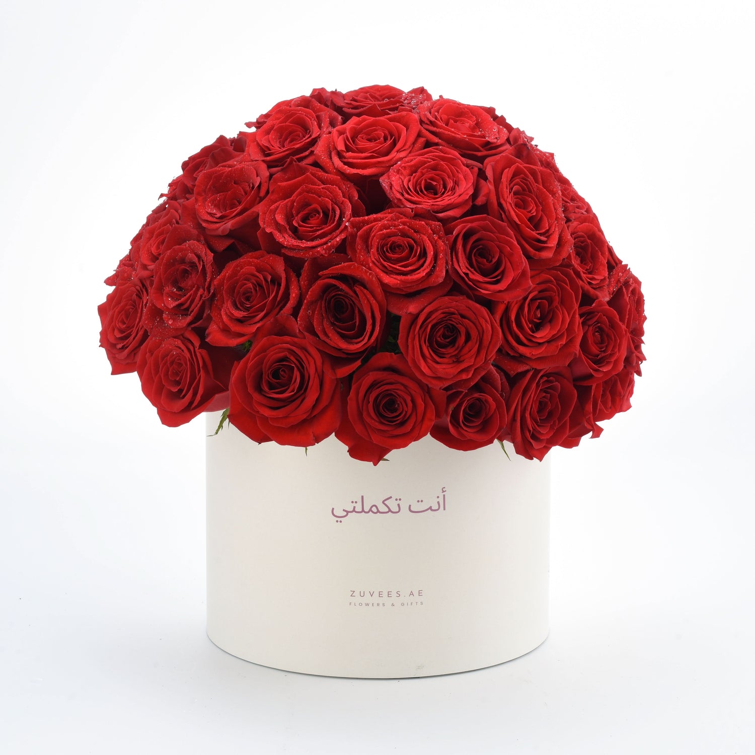 Vibrant red roses in white cylinder box with Arabic message.