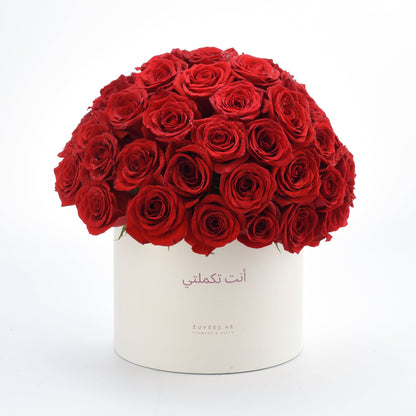 Vibrant red roses in white cylinder box with Arabic message.