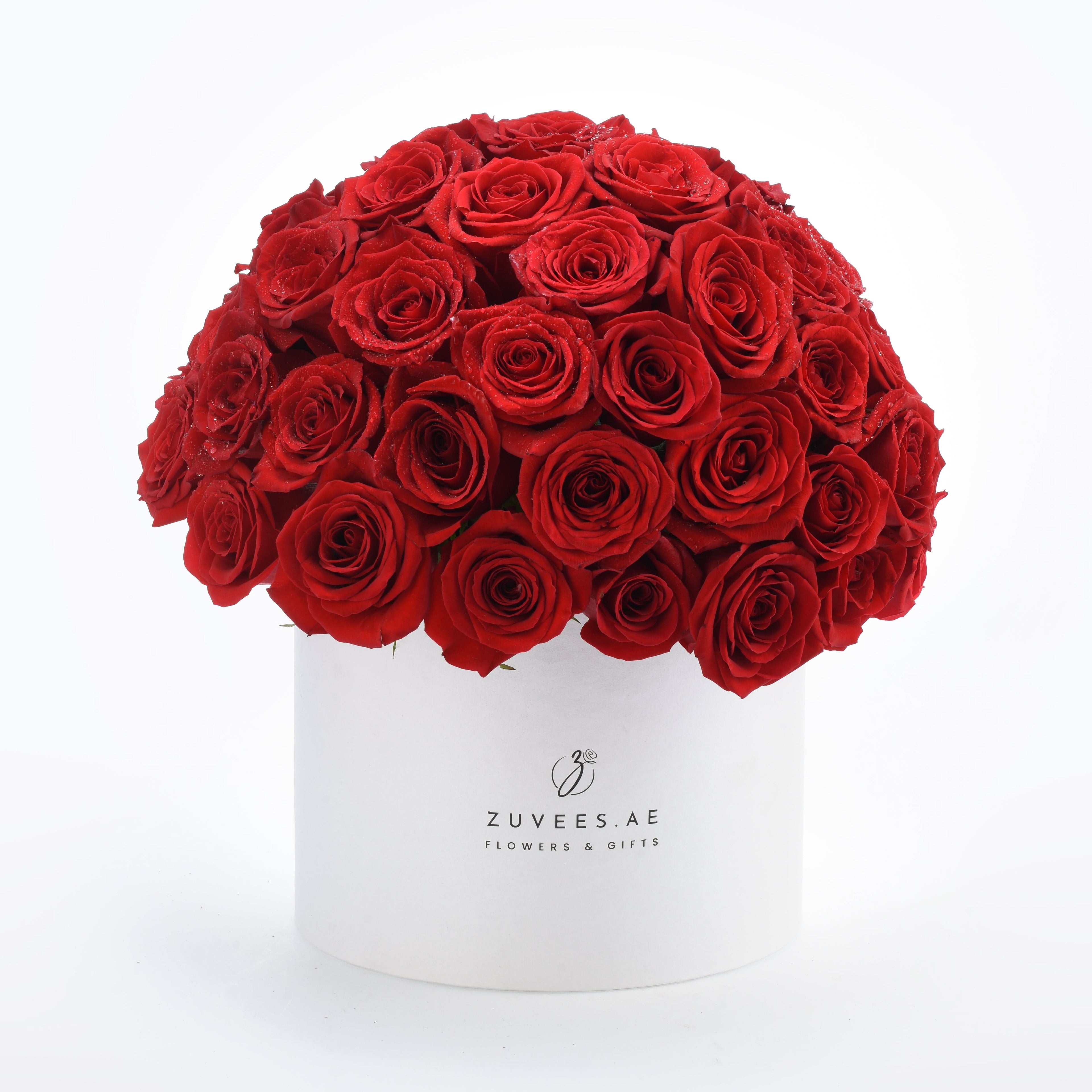 Vibrant red roses in white cylindrical box with "ZUVEES.AE" branding.