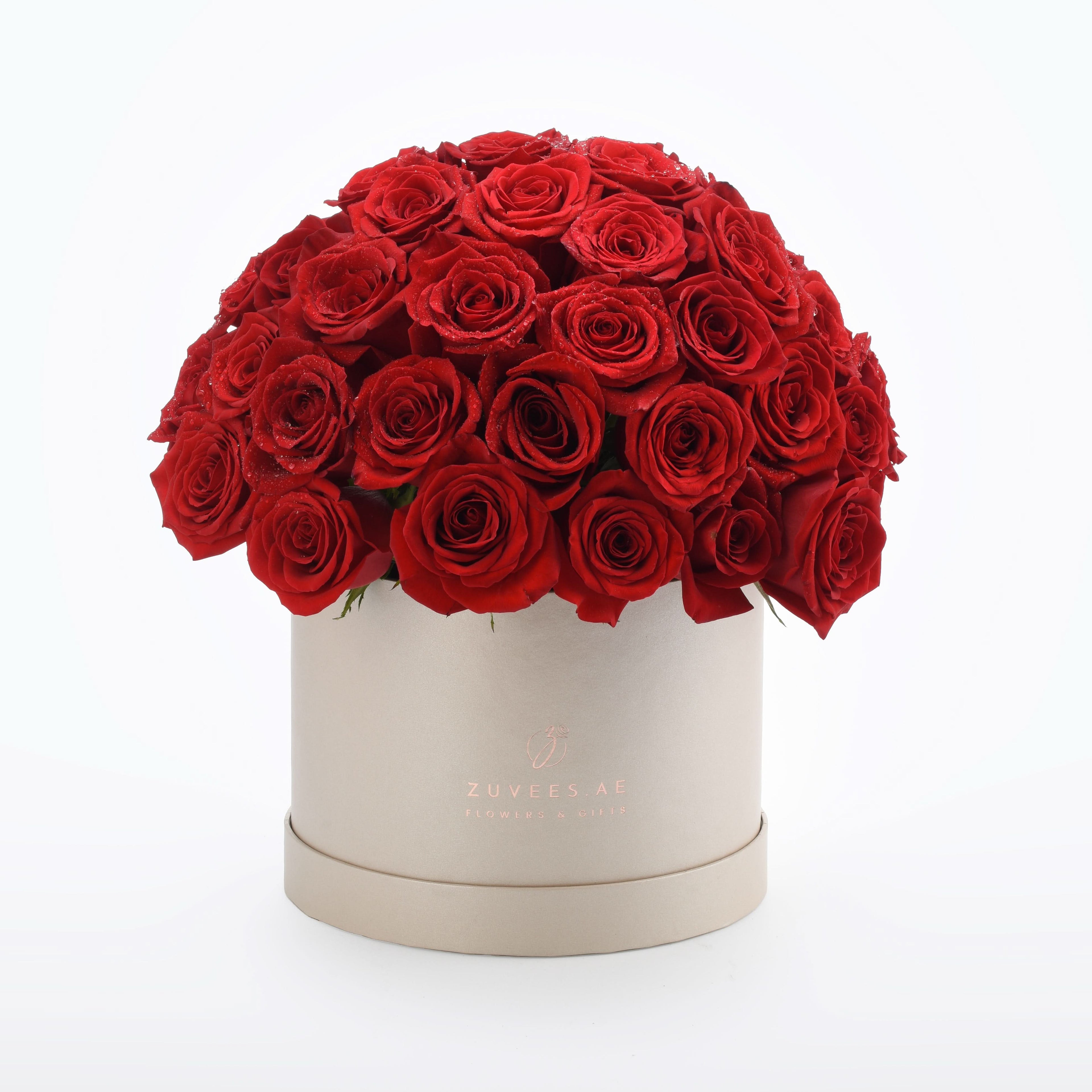 Vibrant red roses in elegant beige box, glistening with dewdrops.
