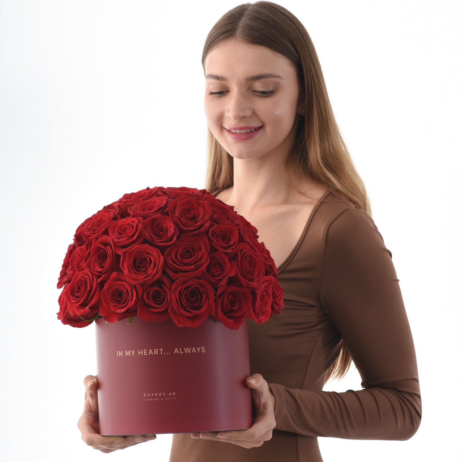 Woman holds deep red roses in matte burgundy box with gold "In My Heart... Always" inscription.