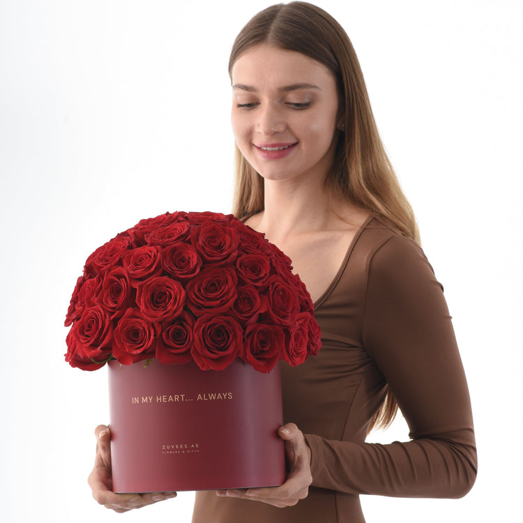 Woman holds deep red roses in matte burgundy box with gold "In My Heart... Always" inscription.