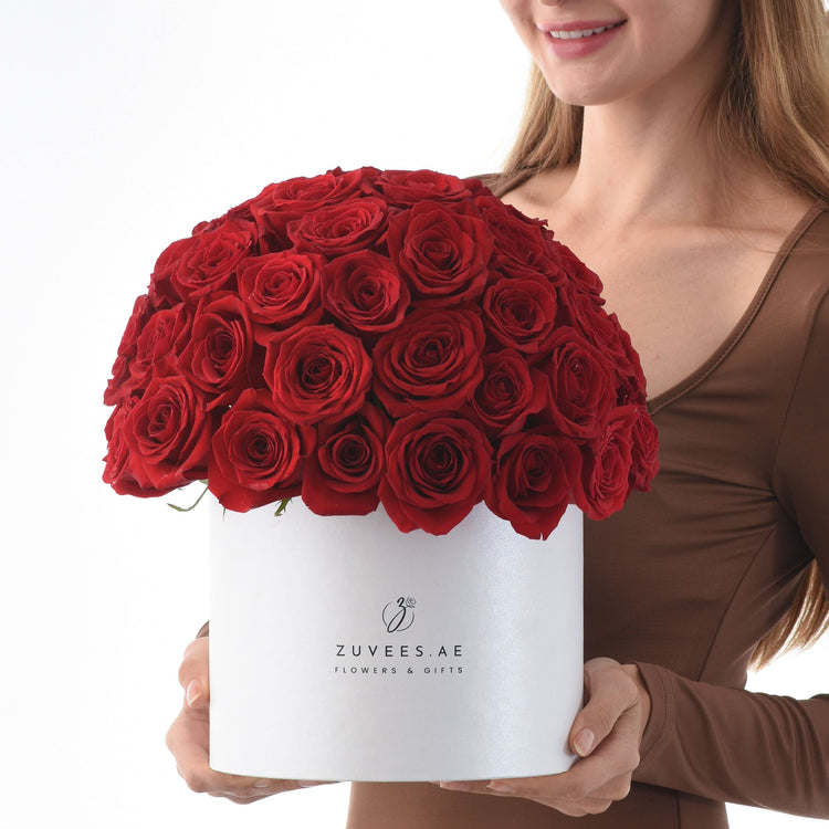 Vibrant red roses overflowing from a sleek white box held by a smiling woman.