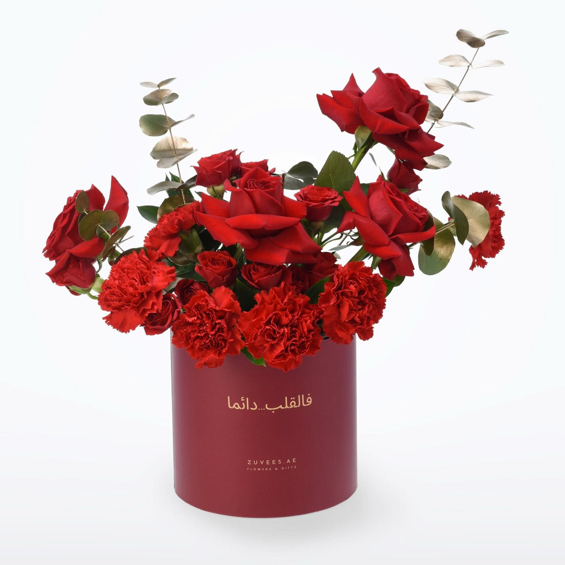 Vibrant red roses and carnations in deep burgundy cylindrical box with gold script.