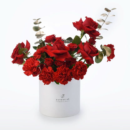 Vibrant red roses and carnations in minimalist white cylindrical vase.