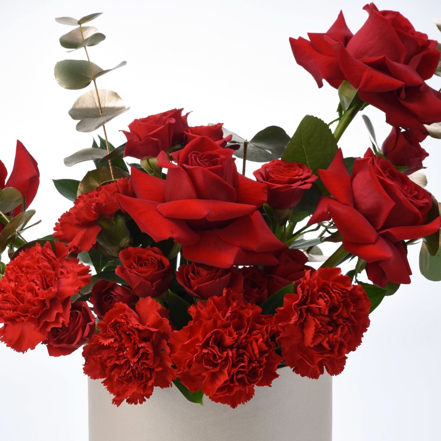 Vibrant red roses and carnations with eucalyptus in sleek white vase, romantic bouquet.