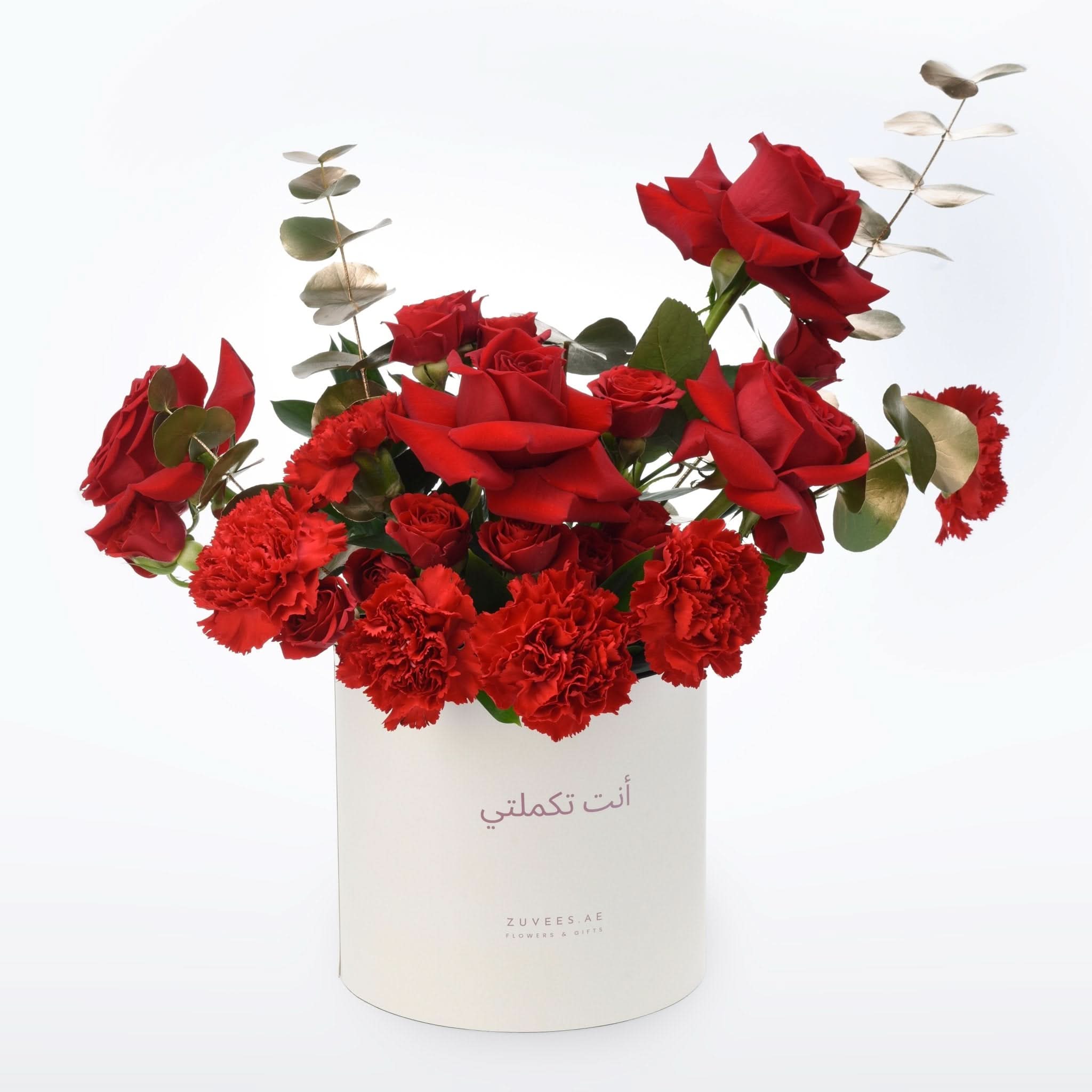 Vibrant red roses and carnations in white cylindrical box with Arabic script.