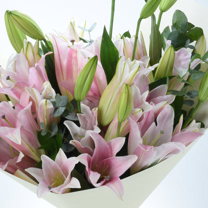 Soft pink lilies with green buds and leaves in cream wrap.