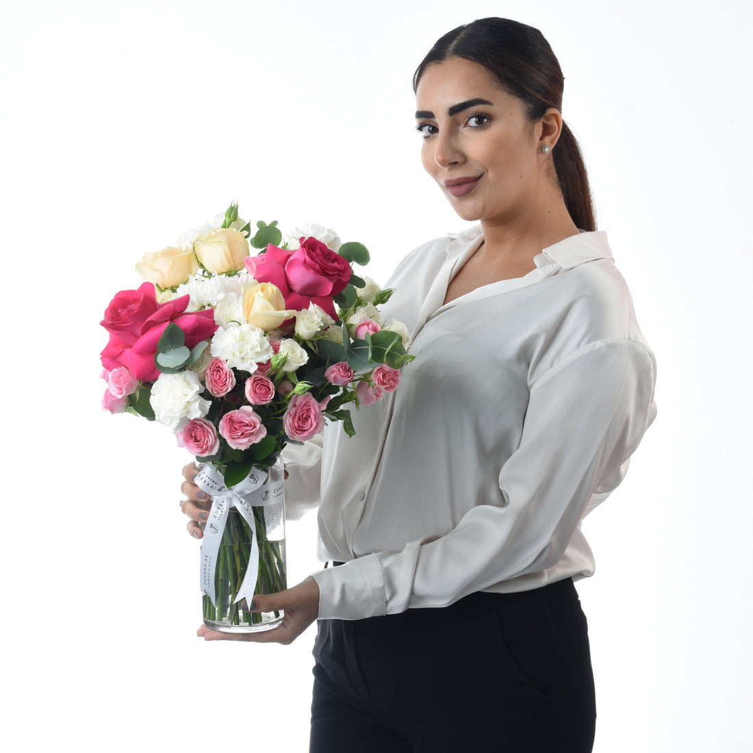 Woman holds vibrant pink, white, and yellow rose bouquet in clear glass vase.