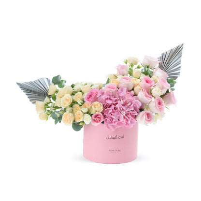 Pink box holds soft roses and hydrangeas, accented with metallic silver wings.