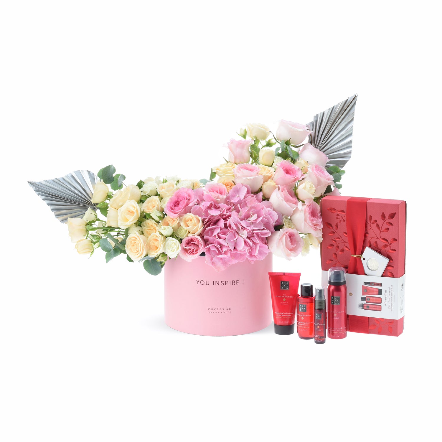 Pink floral arrangement with metallic wings, paired with red Rituals spa gift set.