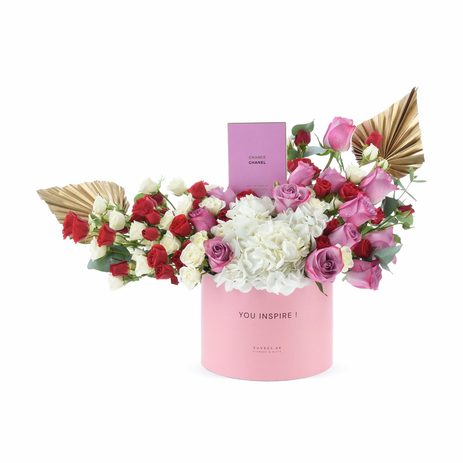 Pink cylindrical box holds vibrant red, white, and pink roses with gold leaf accents and Chanel perfume.