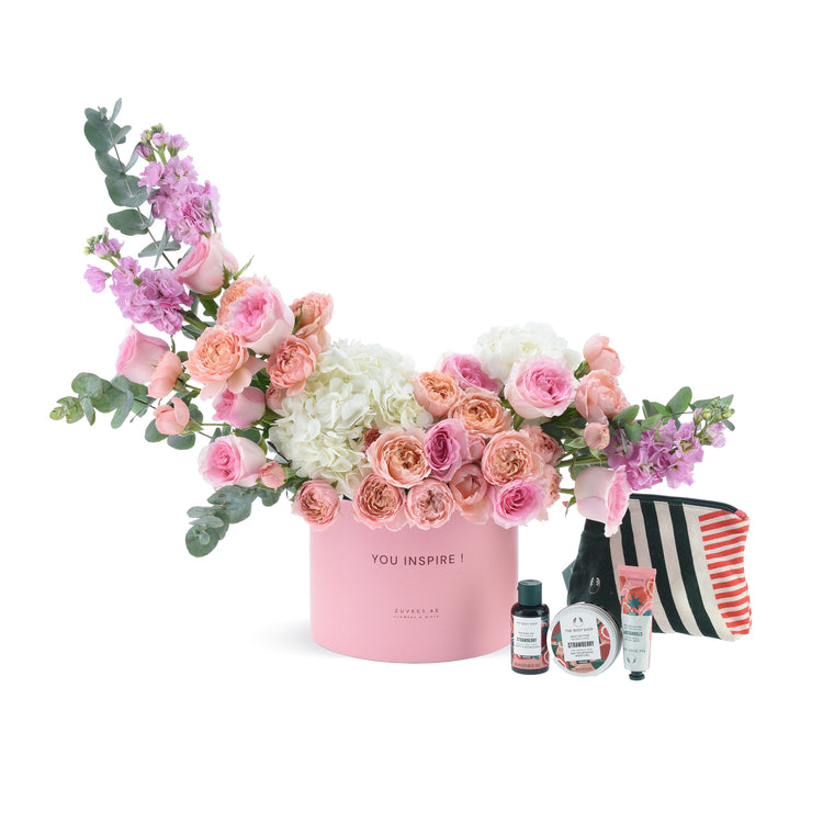Pink floral gift box with roses, hydrangeas, eucalyptus, and strawberry-scented body care set.