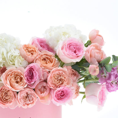 Soft pink, peach, and white roses with hydrangeas in pastel vase.