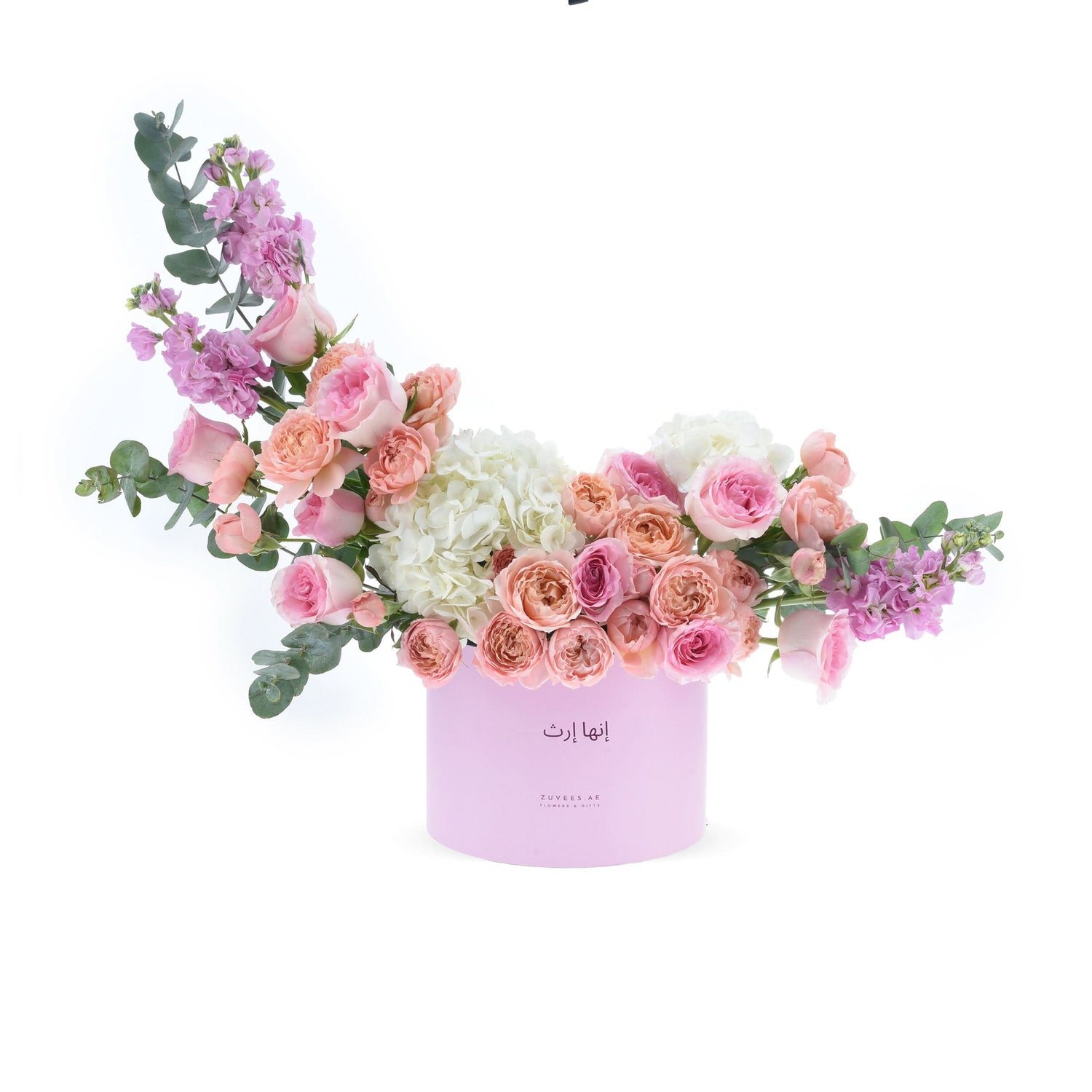 Soft pink roses, hydrangeas, and eucalyptus spill from a lavender gift box.