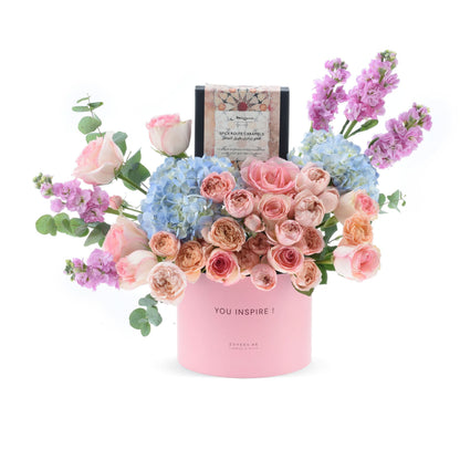 Pink floral arrangement with blue hydrangeas and roses, topped with "YOU INSPIRE!" gift box.