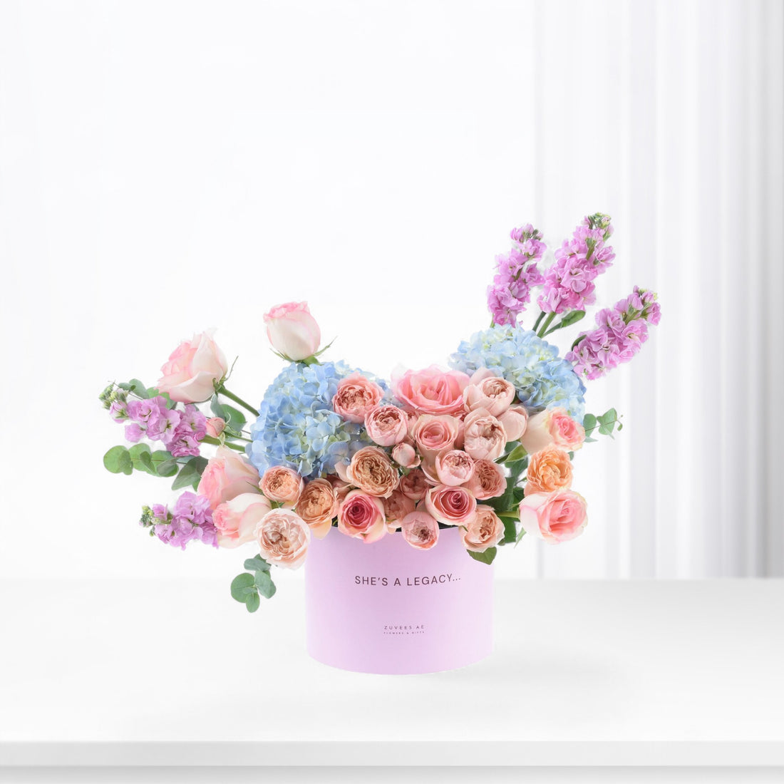 Pastel pink, blue, and lavender floral arrangement in a lavender box with "She&