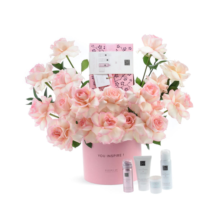 Soft pink roses bloom around a branded pink vase and luxury skincare set.