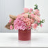 Soft pink roses and hydrangeas bloom in a matte red vase with gold text.