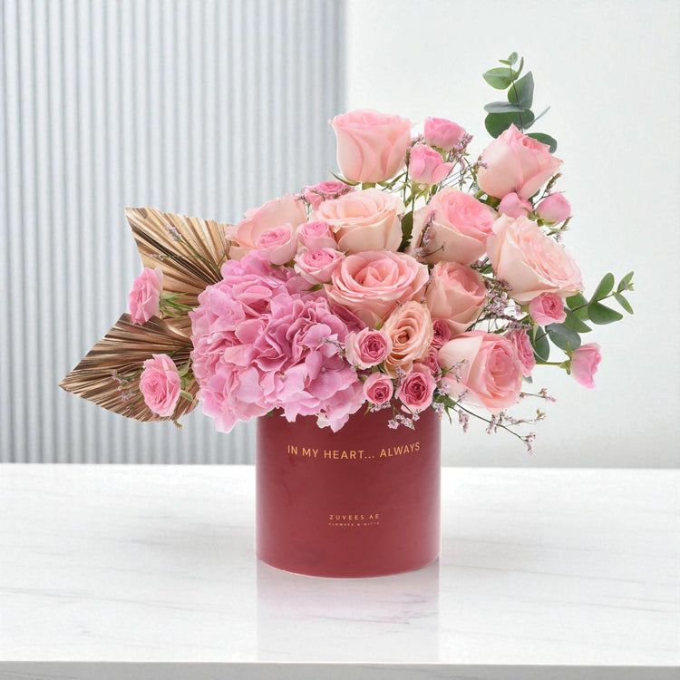 Soft pink roses and hydrangeas bloom in a matte red vase with gold text.