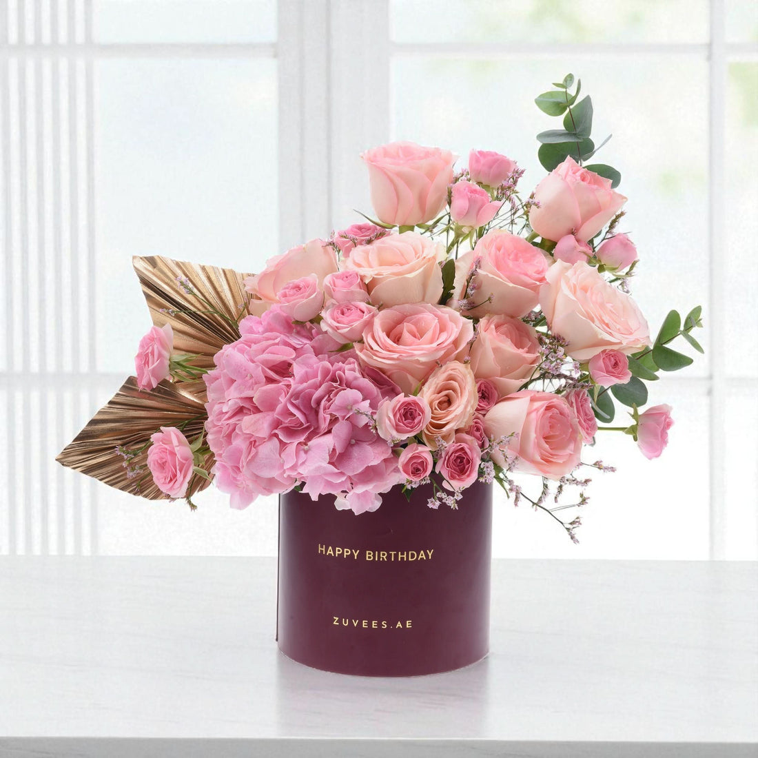 Pink roses and hydrangeas in burgundy box with gold "Happy Birthday" text.