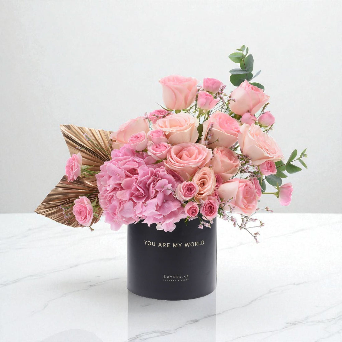Elegant pink rose and hydrangea bouquet in black vase with gold text.