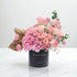 Elegant pink rose and hydrangea bouquet in black vase with gold text.