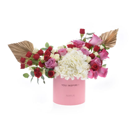 Pink box holds red, pink, white roses and hydrangeas with gold leaf accents.
