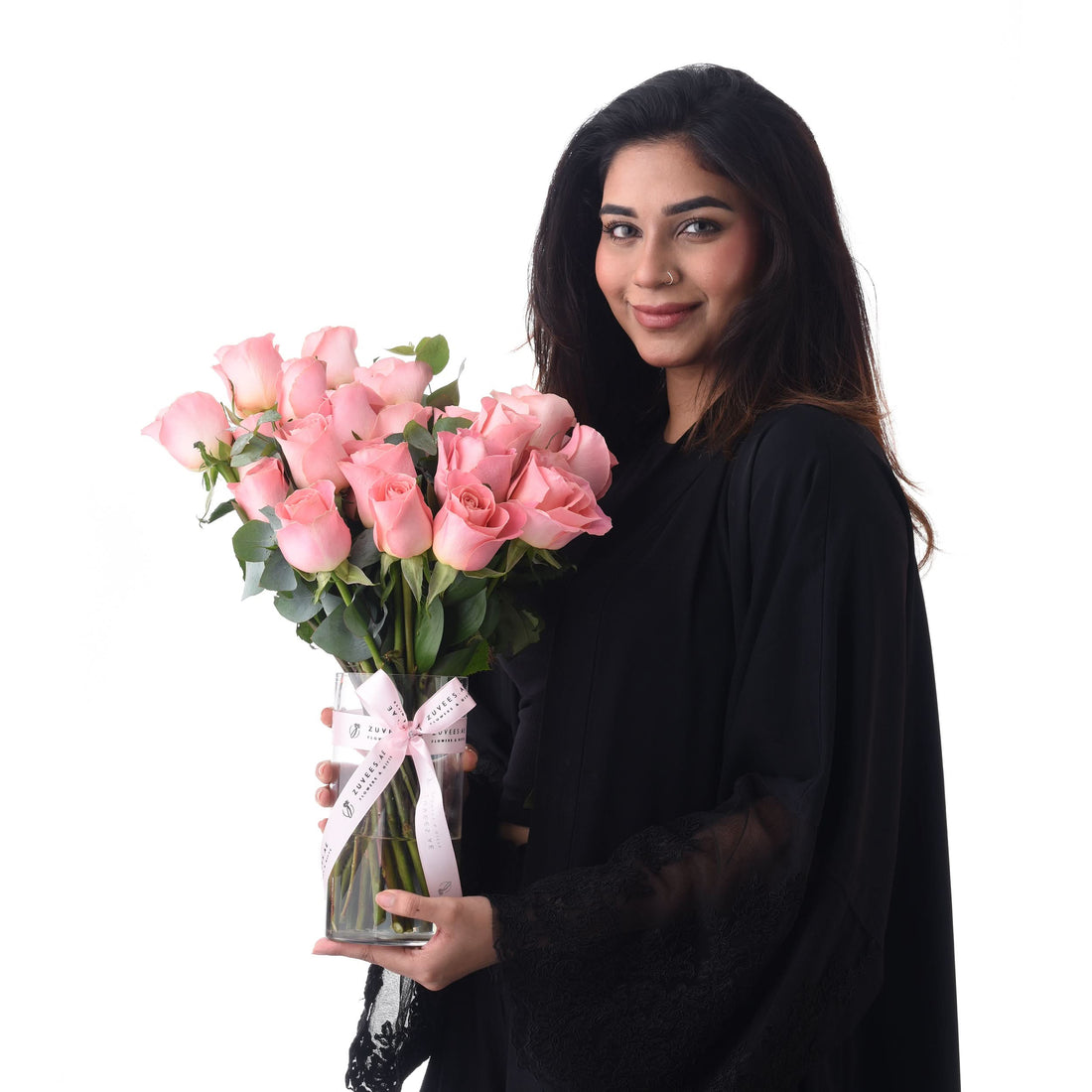 Woman in black holds glass vase of pink roses with branded ribbon.
